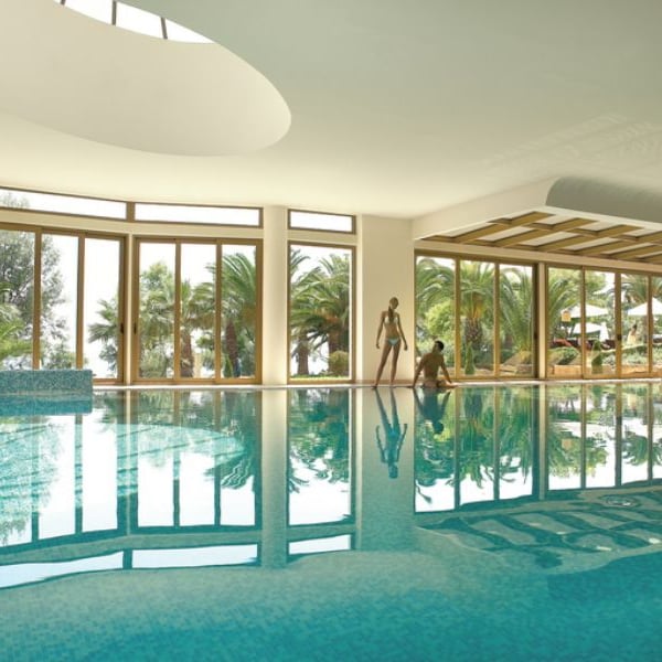 Luxurious indoor pool at Sani Beach with large windows showcasing views of palm trees and reflective blue water.
