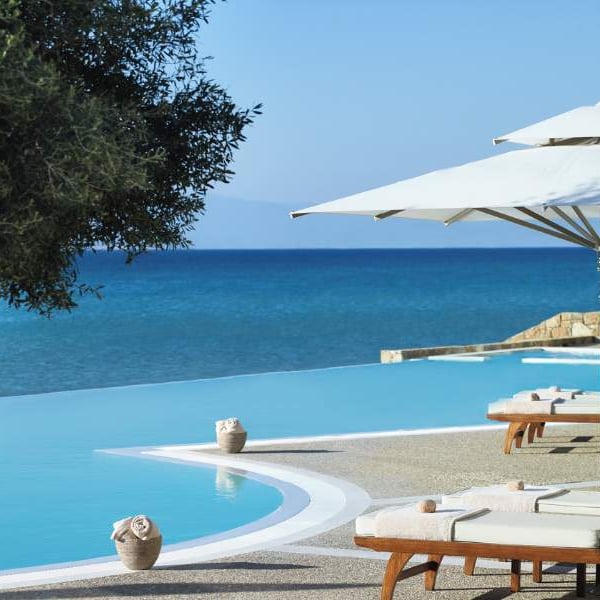 Infinity pool at Sani Beach with sun loungers, umbrellas, and a view of the sea and sky.