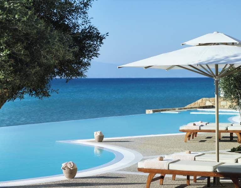 Infinity pool at Sani Beach with sun loungers, umbrellas, and a view of the sea and sky.