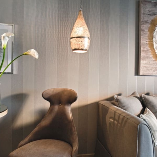 Interior view of a Sani Beach room with grey striped wall, plush grey chair, table with calla lilies, sofa with cushions, and decorative art with hanging light.