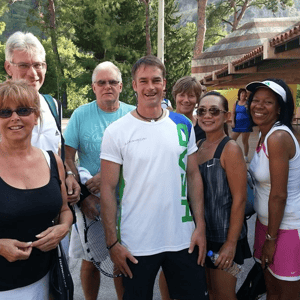 Group of tennis players smiling and posing on a court, holding rackets and wearing casual tennis clothing.