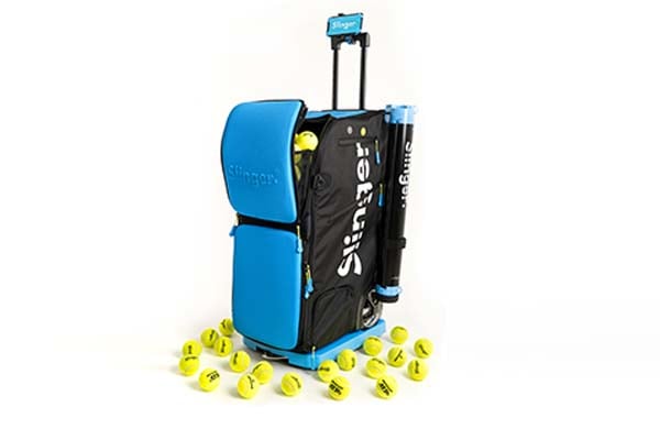 Slinger 2 tennis ball launcher in blue and black, surrounded by tennis balls, illustrating its portability and functionality.
