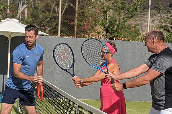 Tennis coach teaching two adults how to hold a tennis racquet on an outdoor court, highlighting interactive coaching methods.