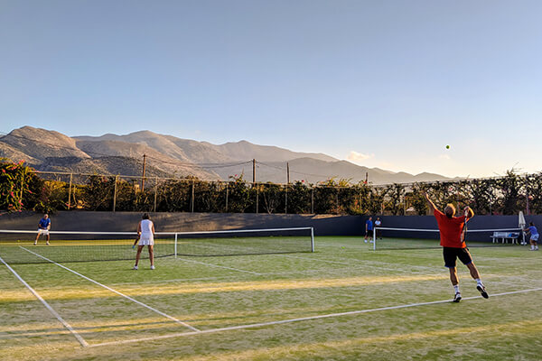 Tennis players in a doubles match on a green court with mountains and clear skies in the background.