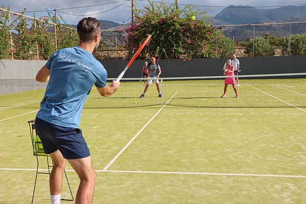 People playing tennis on an outdoor court with a mountain backdrop, ideal for a tennis holiday.