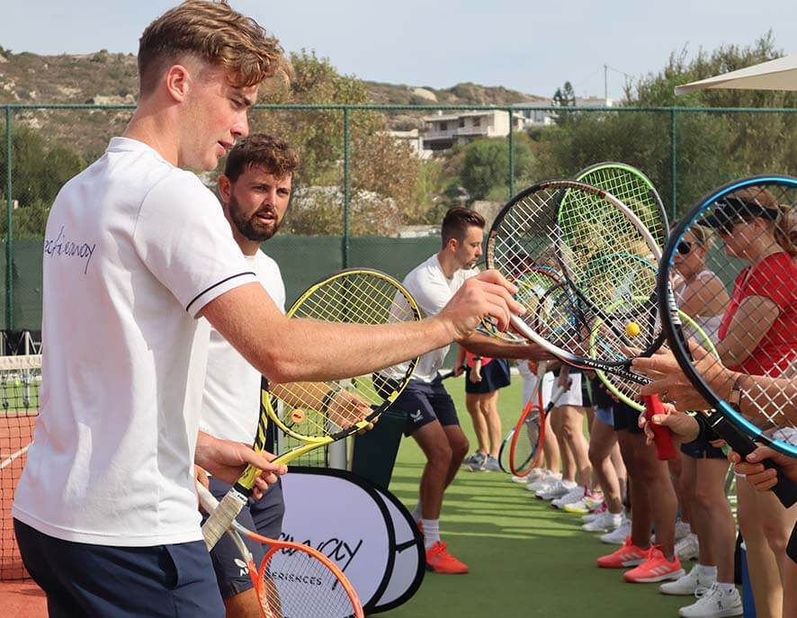 Tennis coach teaching a group of players on a court, players holding rackets and watching attentively.