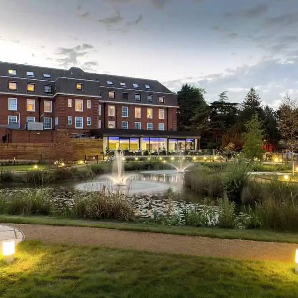 The Lensbury Hotel by the River Thames, showcasing landscaped gardens, a reflective pond, and evening lighting.