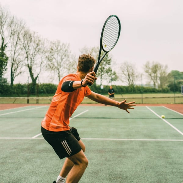 Tennis coach demonstrating technique on the court to a player, highlighting racket control and footwork during practice.