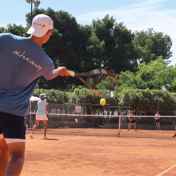 A tennis coach guiding three players on a clay court, surrounded by trees, with a focus on swing techniques.