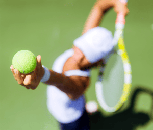 Close-up of a tennis player serving on a green court, focusing on their hand holding a tennis ball and their racket in the background.