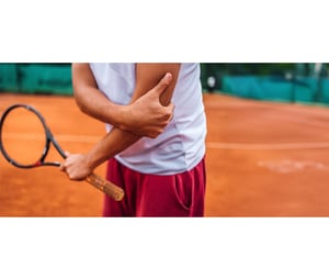 Tennis player holding a racket on a clay court, visible arm suggests muscle tension, wearing white shirt and red shorts.