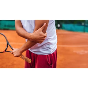 Tennis player holding a racket on a clay court, visible arm suggests muscle tension, wearing white shirt and red shorts.