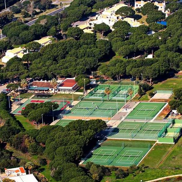 Aerial view of Hilton Vilamoura's tennis courts surrounded by greenery and resort buildings.