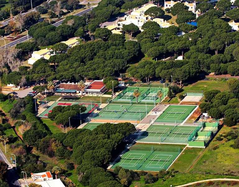 Aerial view of Hilton Vilamoura's tennis courts surrounded by greenery and resort buildings.