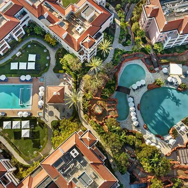 Aerial view of Hilton Vilamoura featuring two large outdoor pools, sun loungers, landscaped gardens, and hotel buildings.