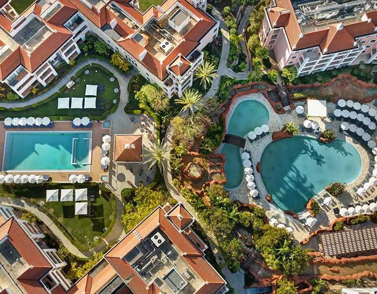 Aerial view of Hilton Vilamoura featuring two large outdoor pools, sun loungers, landscaped gardens, and hotel buildings.