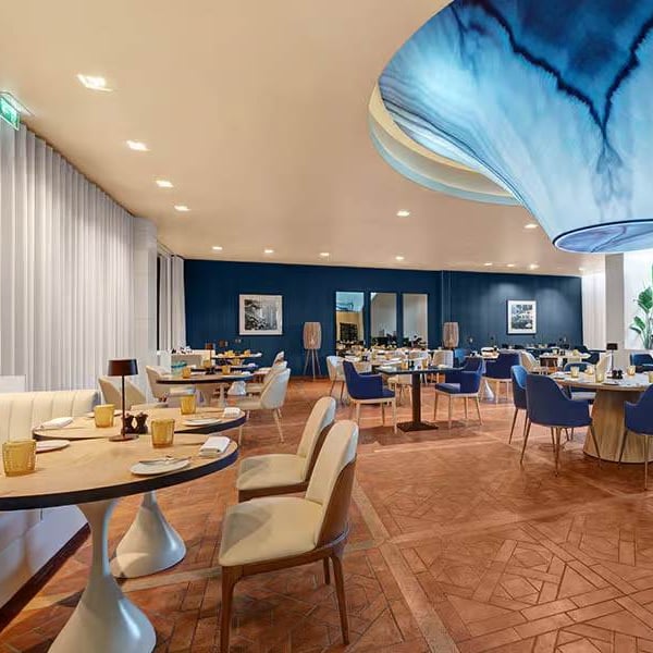 Indoor dining area at Hilton Vilamoura showcasing elegant decor with blue and beige chairs, parquet flooring, and a unique blue wave ceiling fixture.