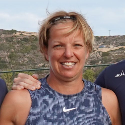 Lucy, wearing a navy blue sports top, smiling outdoors with hills and clear sky in the background.