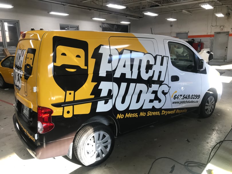 White compact cargo van with bold yellow and black drywall-service graphics