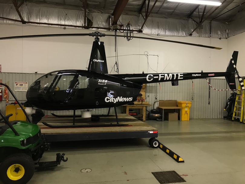 White CityNews logos, aircraft registration, and safety labels on a black helicopter in a hangar