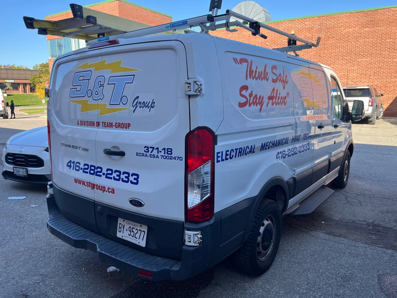 Rear and passenger side of an S and T Group service van with company logos, service lettering, phone number, and safety slogan