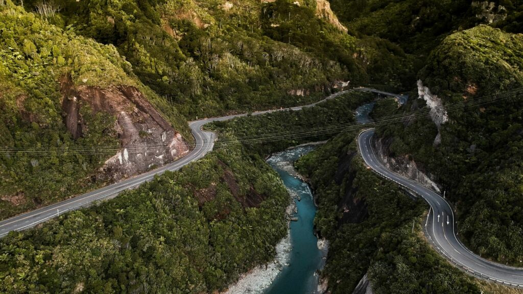 A road going down a valley with turns, green nature around and a river in the middle of the valley