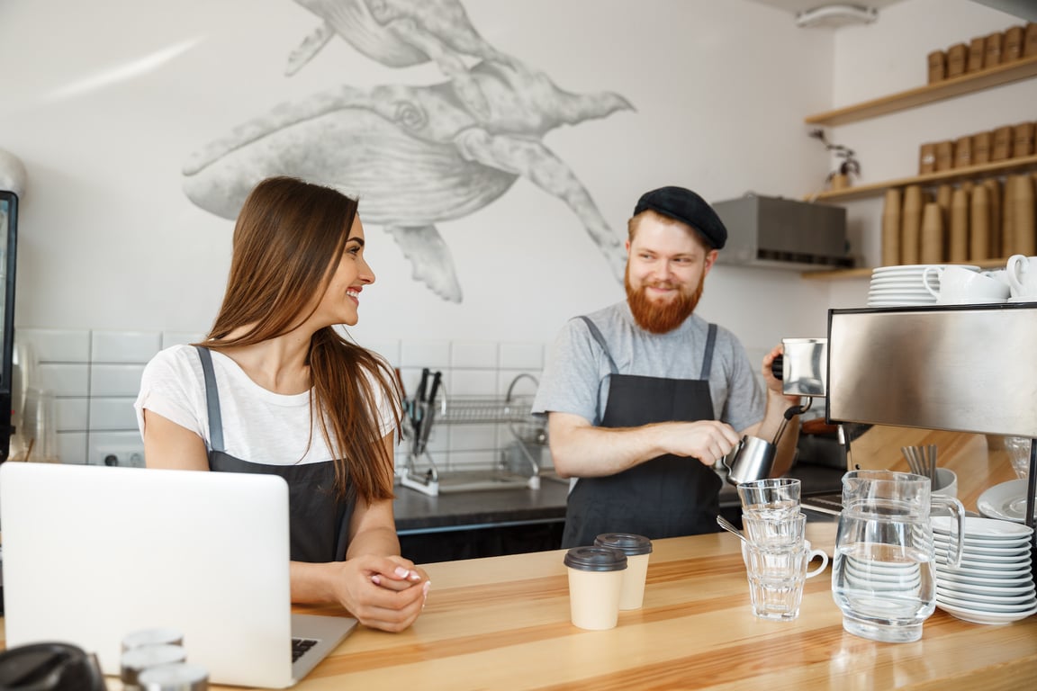 Coffee Business Concept - Positive young bearded man and beautiful attractive lady barista couple enjoy working together at the modern coffee shop