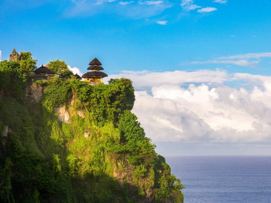 Uluwatu Temple on the top of a green cliff going down in the ocean