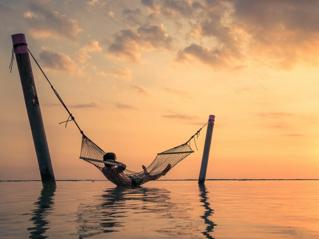 Man laying in a hammock in the ocean enjoying the sunset