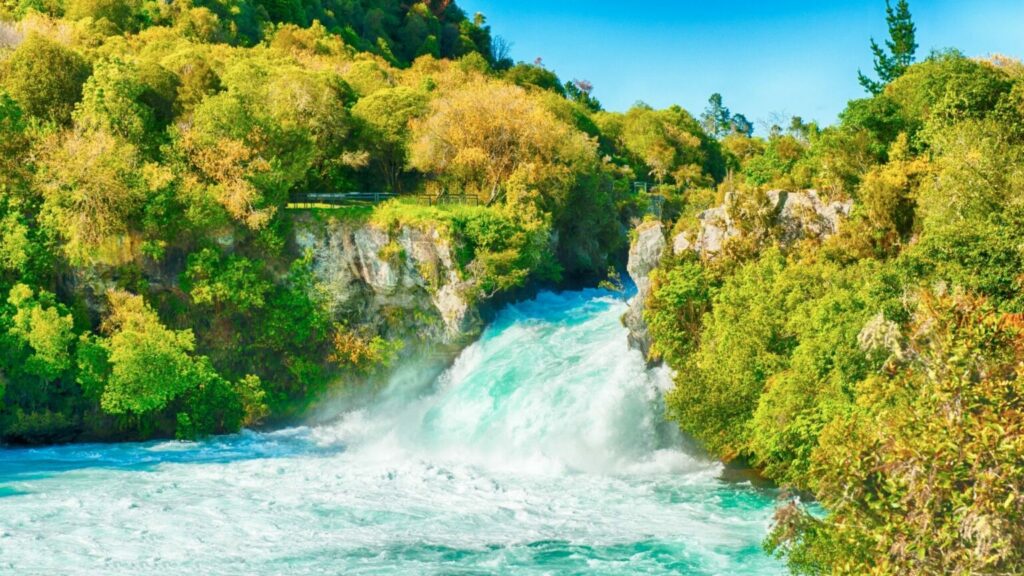 Waterfall in Huka Falls with blue water and green trees surrounding the waterfall