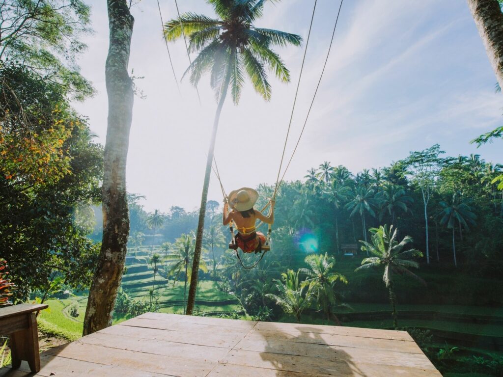 Woman on a swing in Bai, surrounded by palmtrees, lush nature and a wooden terrace