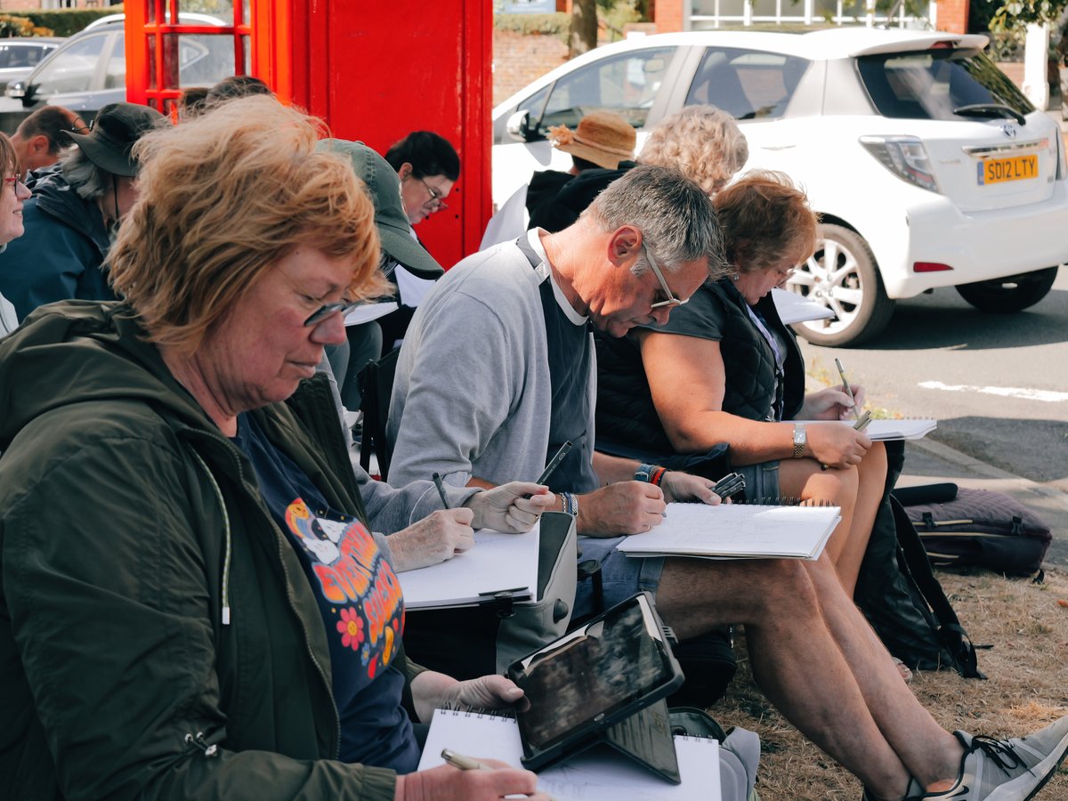 Urban sketching students drawing outdoors on a British street, with a red telephone box behind them.