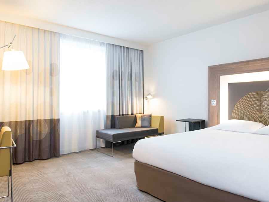 A bedroom at the Novotel Brussels City Centre, with a large window, seating and a double bed