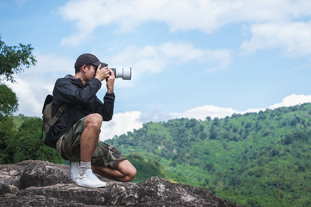 Photographer sits on a cliff with a beautiful mountain landscape in the background. Travel concept adventure active vacations outdoor