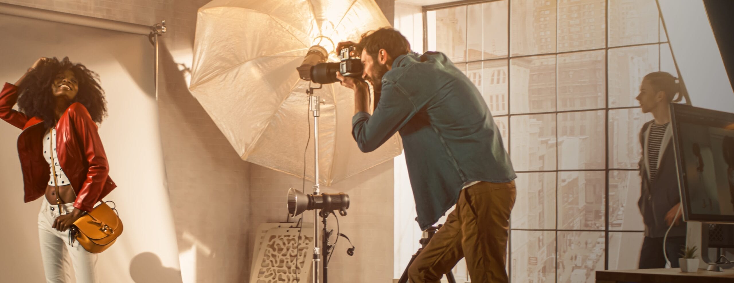 A photographer in a studio taking a photo of a young female model wearing a red leather jacket surrounded by lights