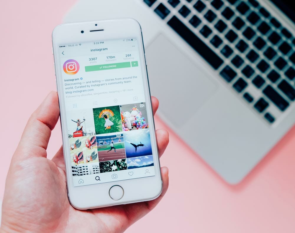 Hand holding Apple iPhone6s with Instagram application on the screen with laptop background. Instagram is a photo-sharing app for smartphones.