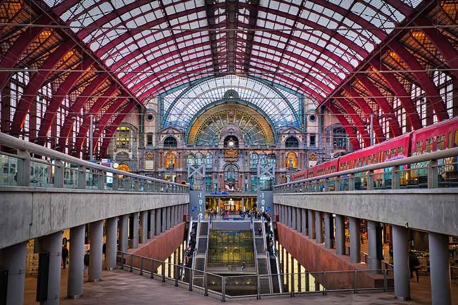 The great hall of Antwerpen-Centraal station, with red steel arches supporting a vaulted glass roof above the platforms