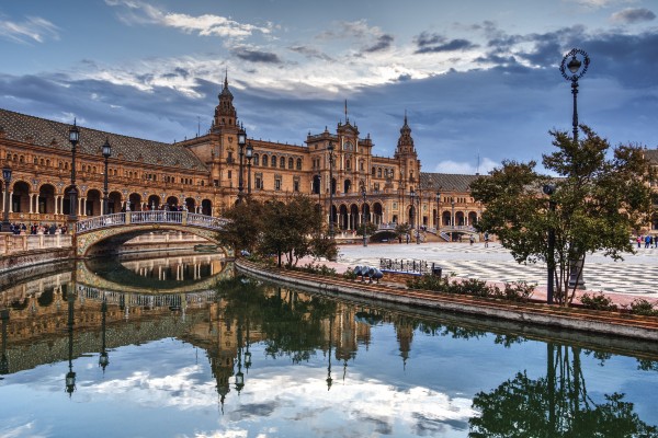 The Plaza de Espa&ntilde;a in Seville, Spain, reflected in its canal at golden hour &mdash; the F/65 Group workshop destination.