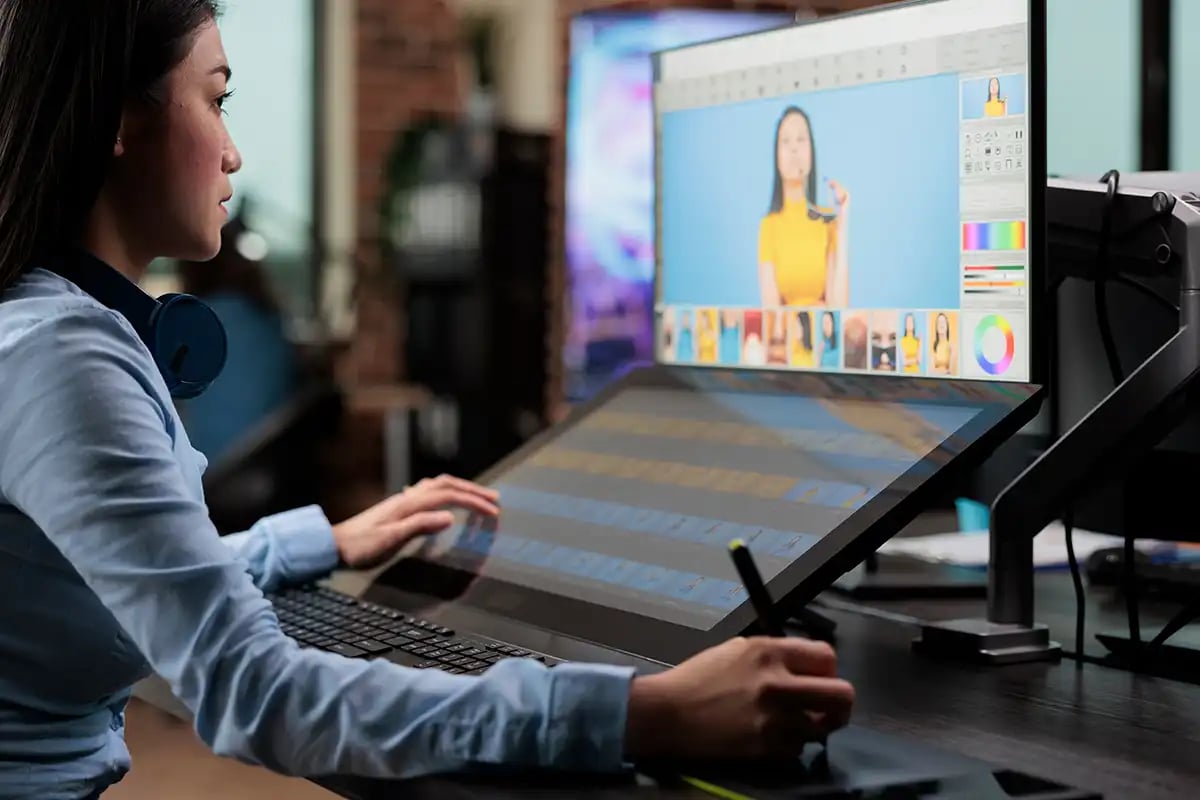 A digital retoucher sat at a desk retouching photos on a computer using a graphic stylus pen