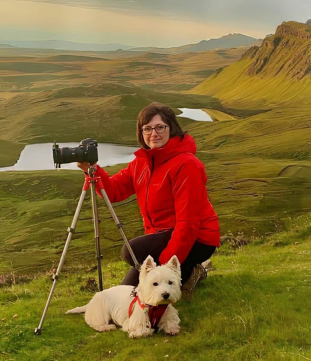 Deborah McPhail in the Scottish Highlands with her DSLR on a tripod and her West Highland Terrier beside her.