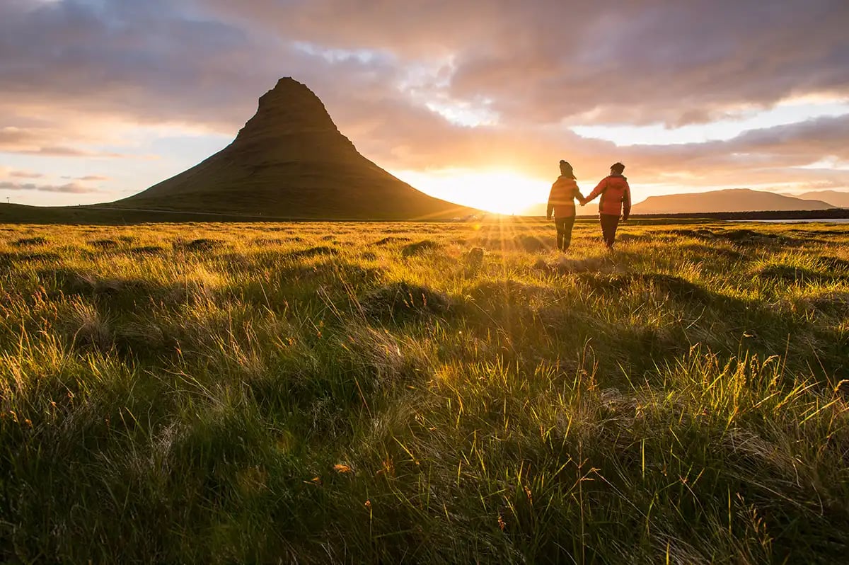 Sunset behind a mountain with two people walking in a field holding hands