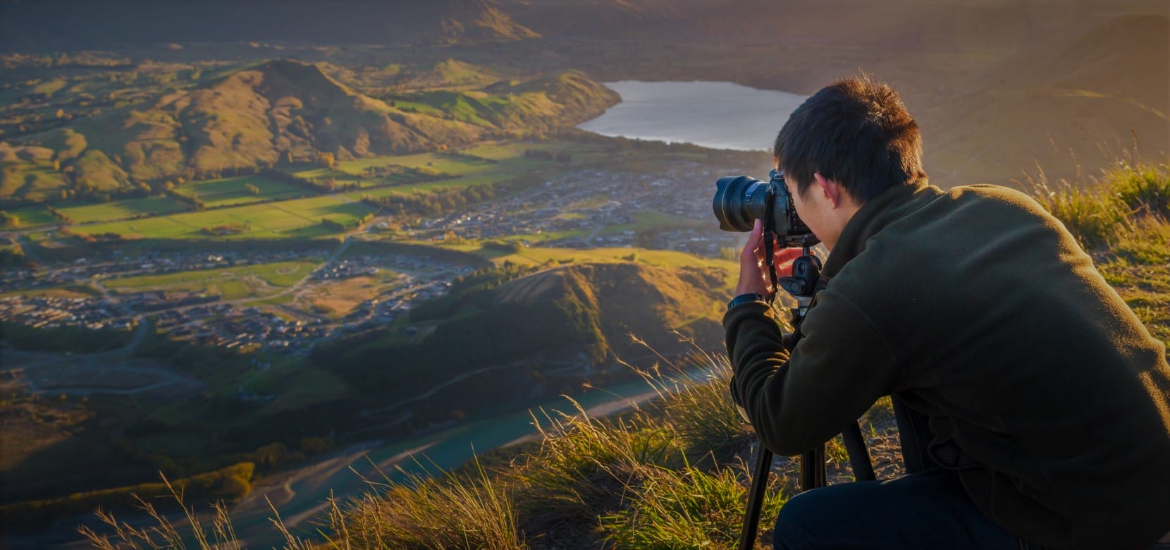a photographer looking through the camera eyepiece taking a photo of a valley below in early morning
