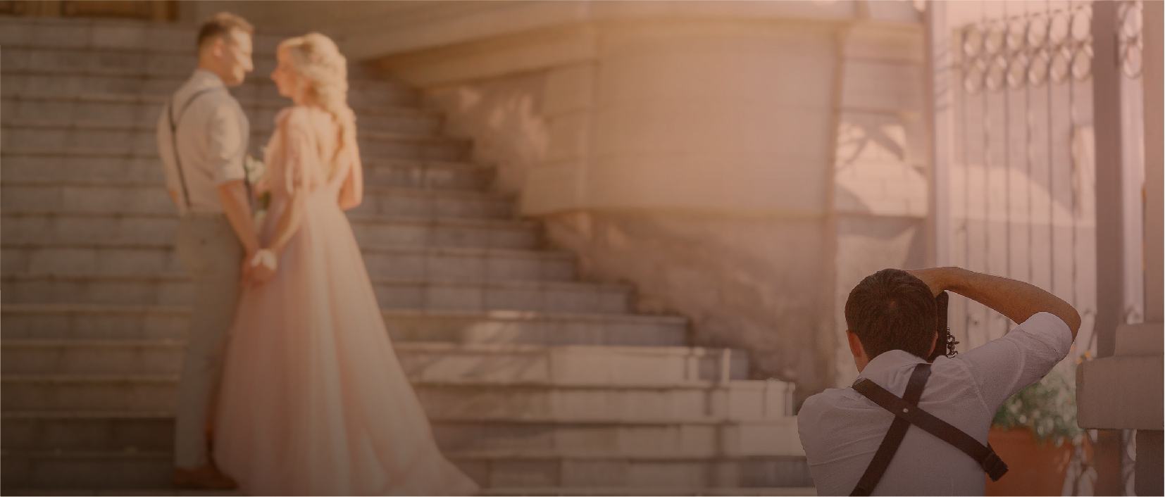 A wedding photographer crouched down taking a photo of a bride and groom holding hands at the bottom of some stairs.