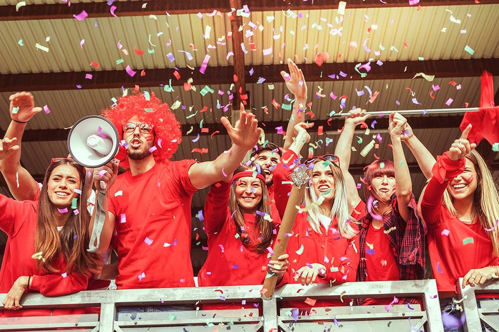 group of fans dressed in red color watching a sports event in the stands of a stadium