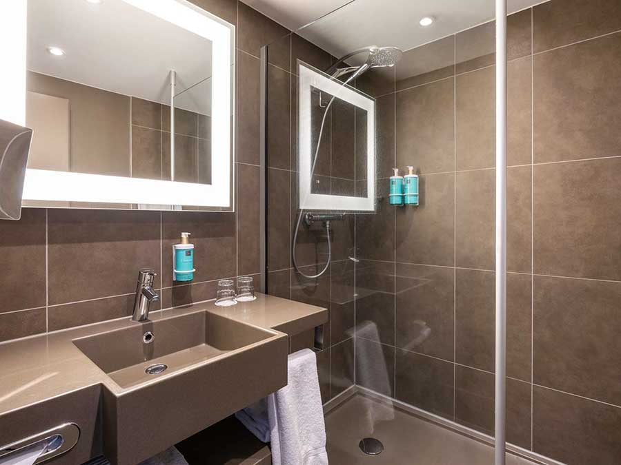 An en-suite bathroom at the Novotel Brussels City Centre with a walk-in shower and lit mirror