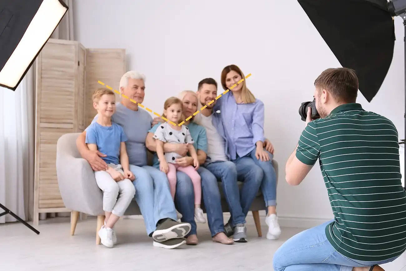 a family sat on a grey sofa cuddled together with children on their laps having their photos taken by a photographer with two lights either side of him