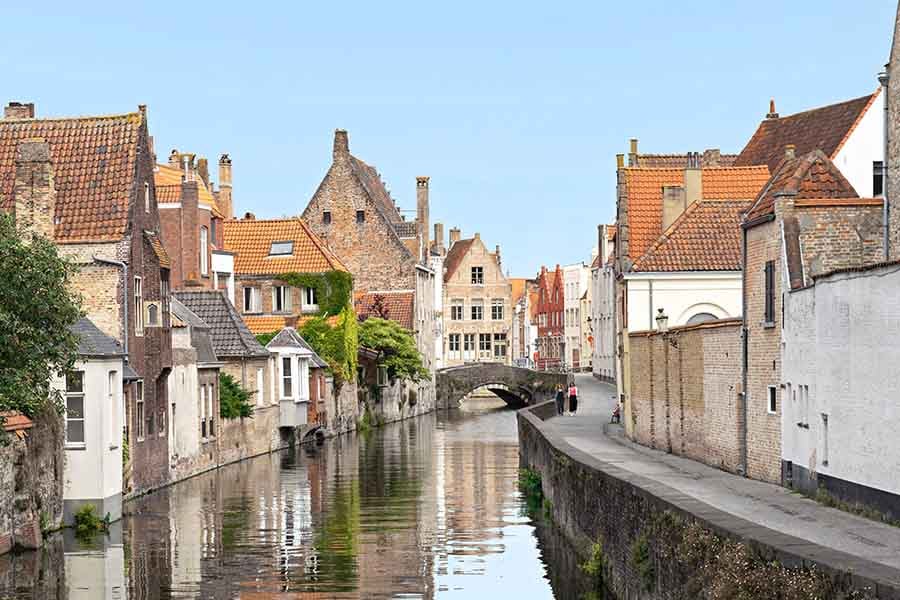 A quiet canal in Bruges with a low stone bridge and stepped-gable houses reflected in still water