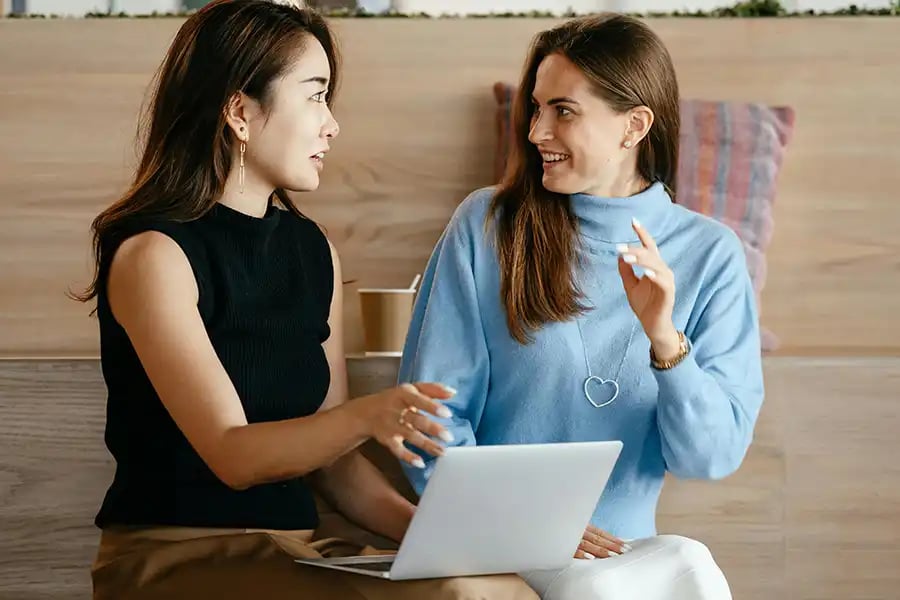 two woman sat talking with a laptop on their knees