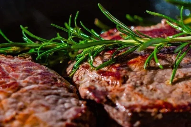 Close-up of sliced medium-rare steak with seared crust and pink interior, garnished with rosemary and served on a wooden cutting board—photographed by Idaho Photography Studios.
