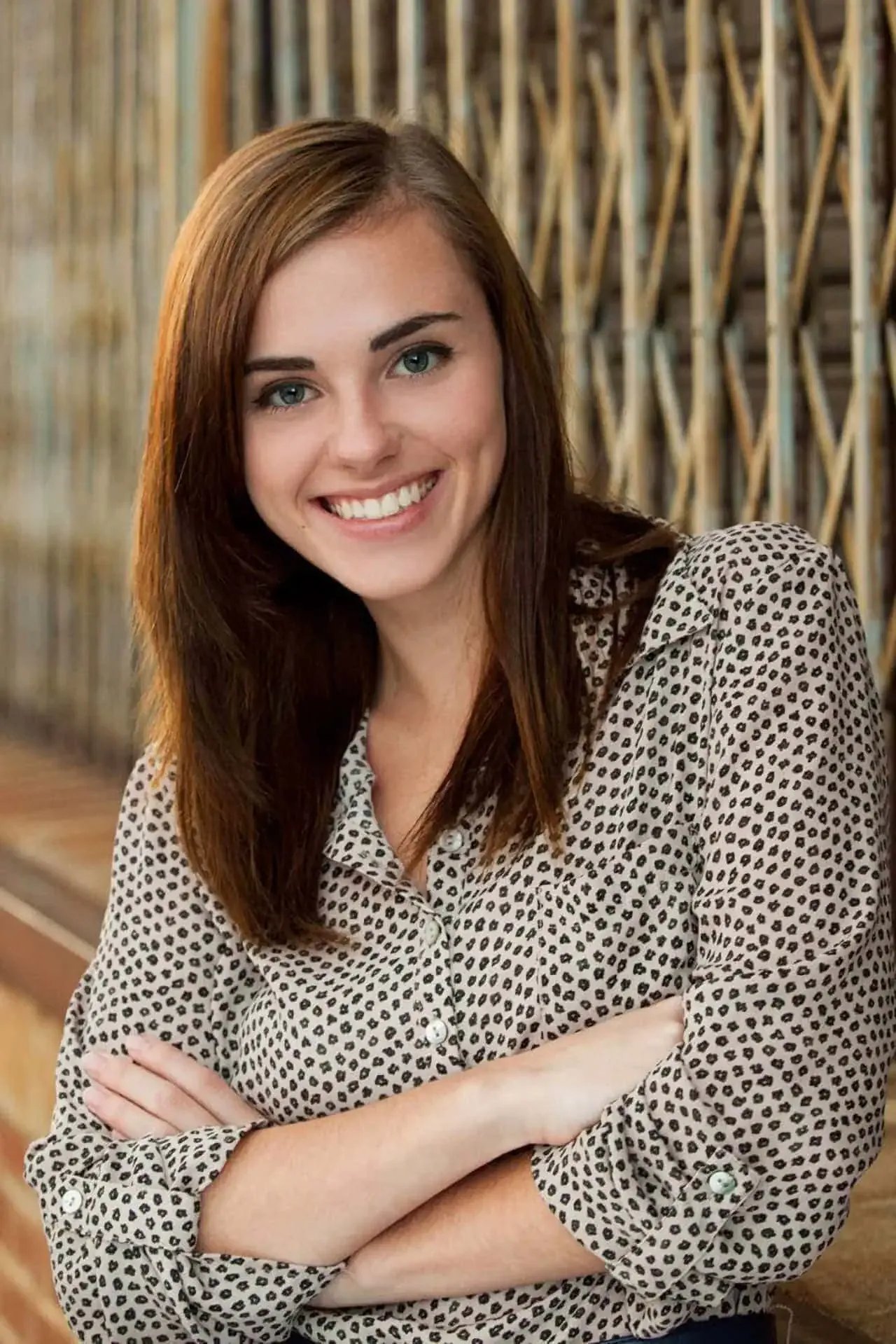Caldwell High senior standing in front of a metal gate and brick wall, smiling with arms crossed in a patterned shirt